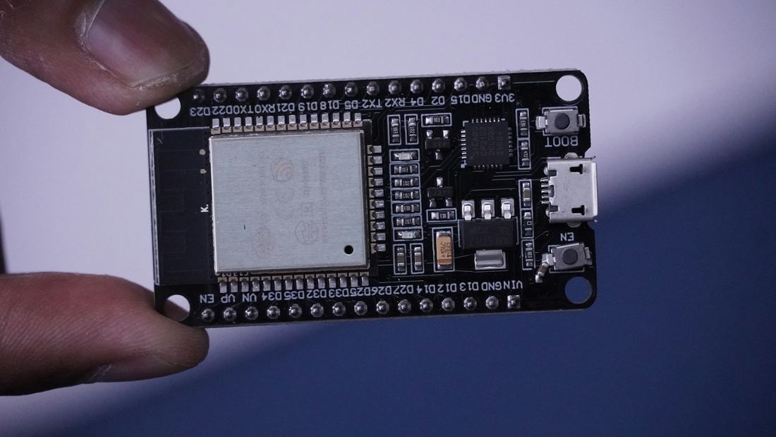 Placa de desenvolvimento ESP32 segurada entre os dedos